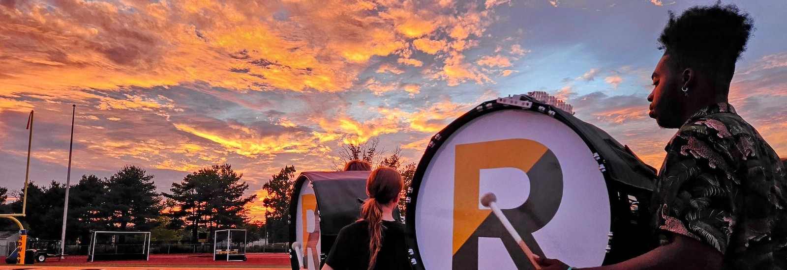 A close up of the Rowan University marching band drum major practicing on the athletic field with a dramatic sunset in front of him.