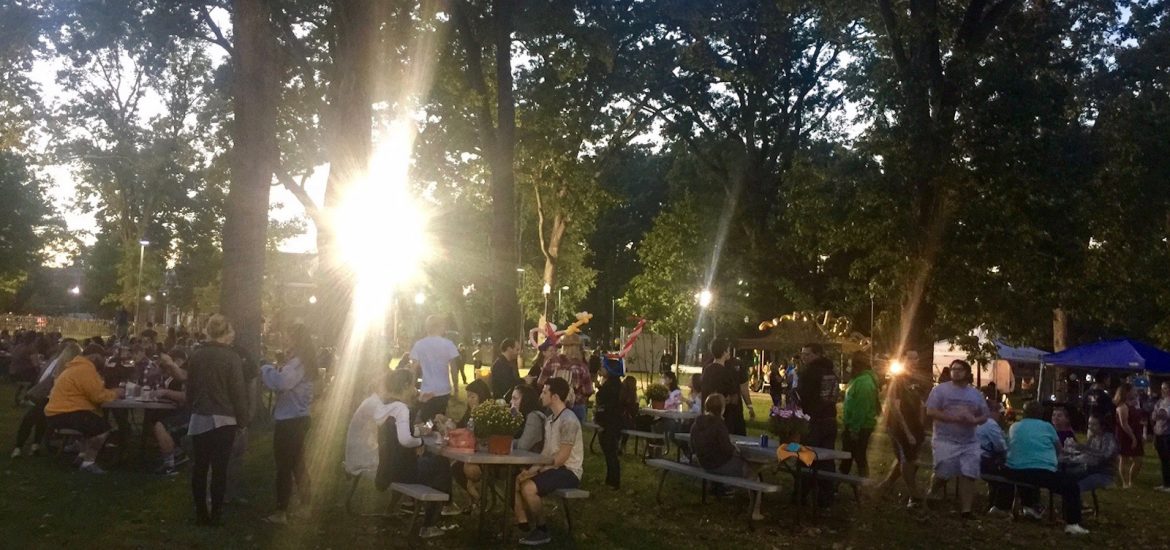 sunlight steams through trees to illuminate students sitting at tables at Homecoming block party