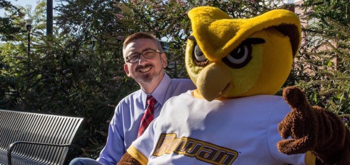 Senior Vice President Jeff Hand sits on a bench with the Rowan mascot giving a thumbs up