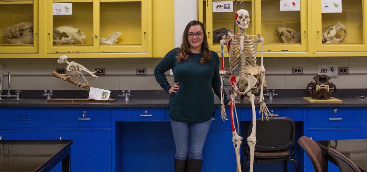 student sits in museum lab next to skeleton