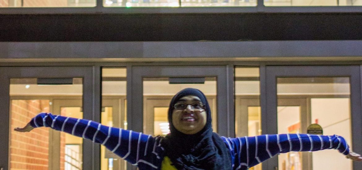 Naveen stands arms outstretched in front of stained glass at James Hall