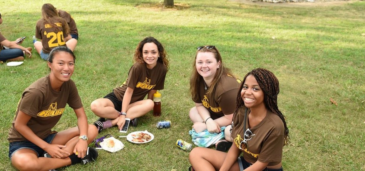 four girls wearing brown Rowan t-shirts sit on the grass