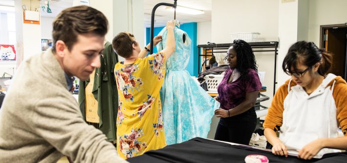 Three students and the costume shop professor work together pinning curtains