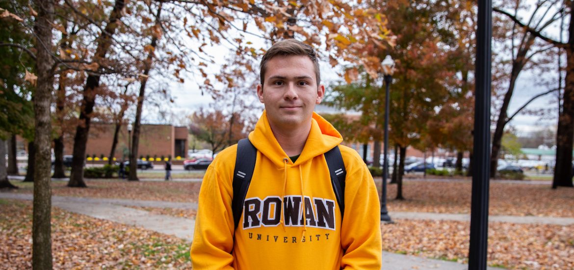 student in Rowan hoodie outside in front of fall leaves and trees