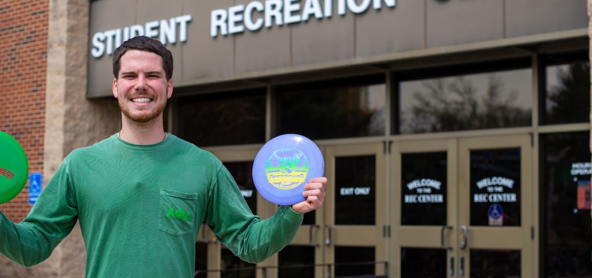 Austin out front of the Rec center holding frisbees up outside