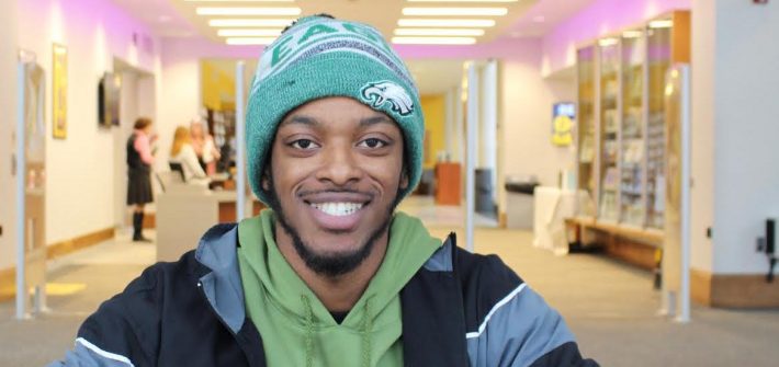 Jamal sitting in the library with a green beanie on.