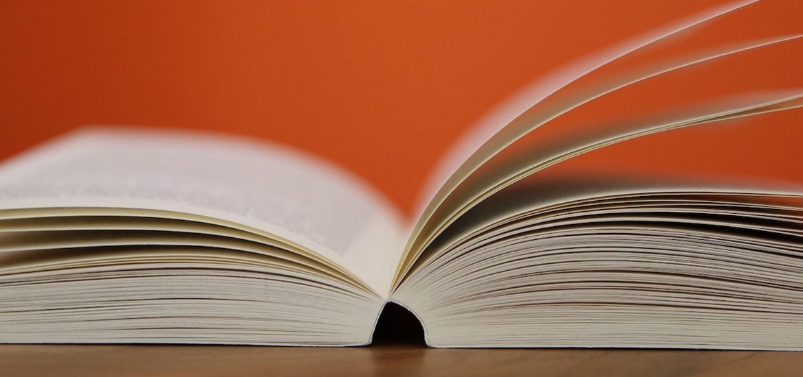 Stock image of an open book fanned against an orange background.
