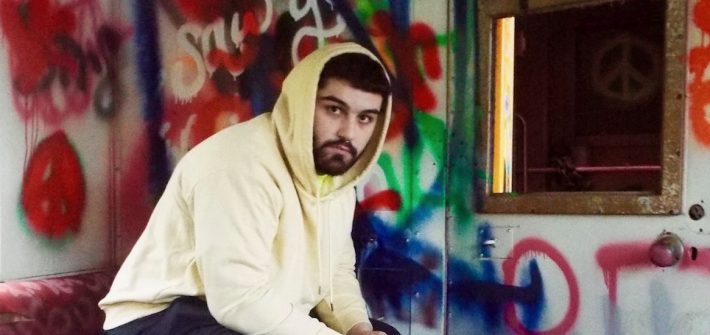 Photo of Frank Ziegler wearing a hooded sweatshirt sitting in a graffiti-covered room
