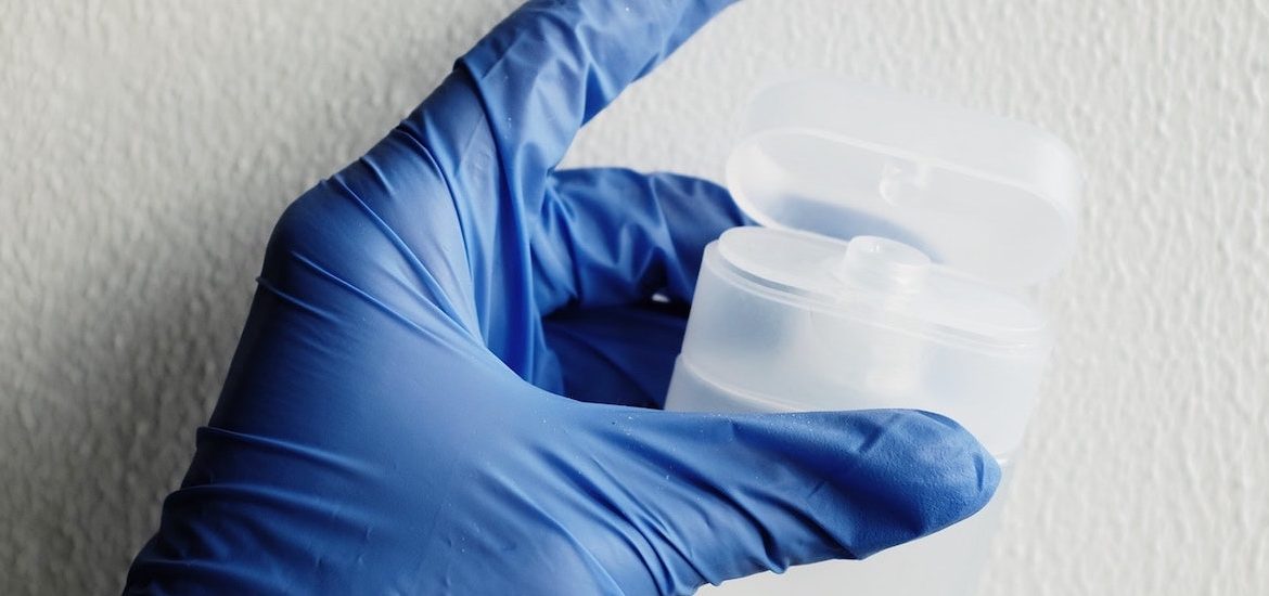 Stock photo of a hand covered with a blue medical glove holding a plastic container.