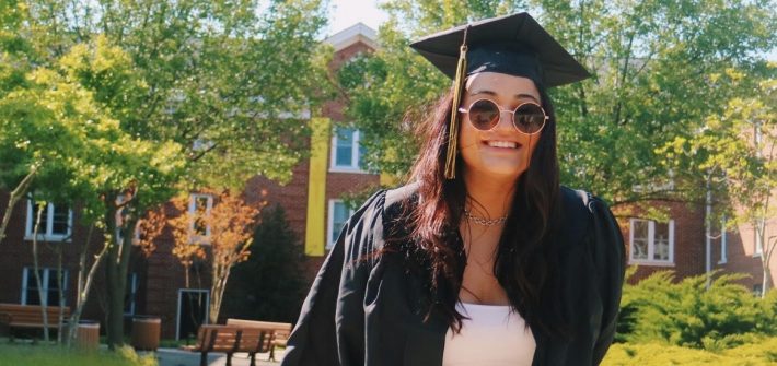 Gianna poses in front of a freshman residence hall in her graduation regalia.