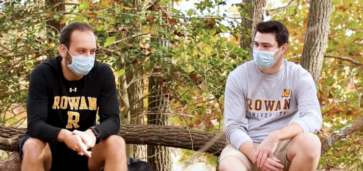 Two students in Rowan gear sit at the nature preserve.