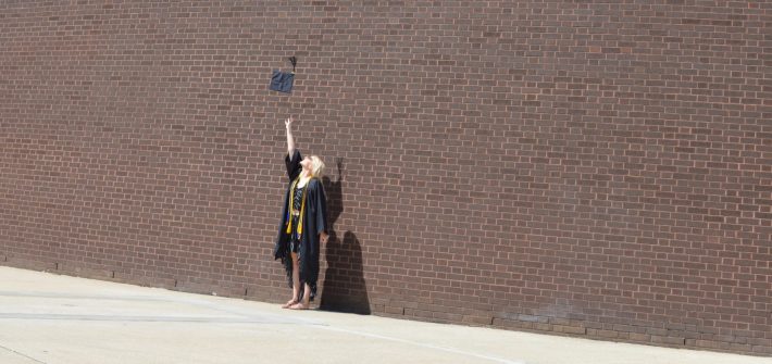 Amanda wears a cap and gown in front of a brick building.