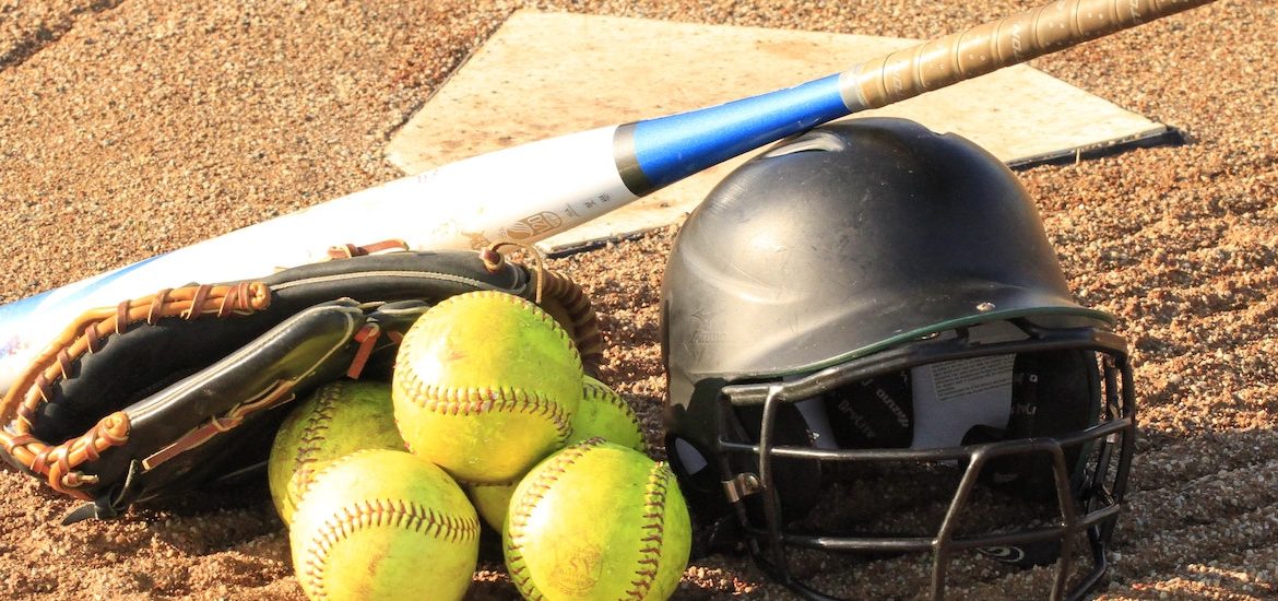 Stock image of a softball home plate with a helmet, three softballs and a bat.
