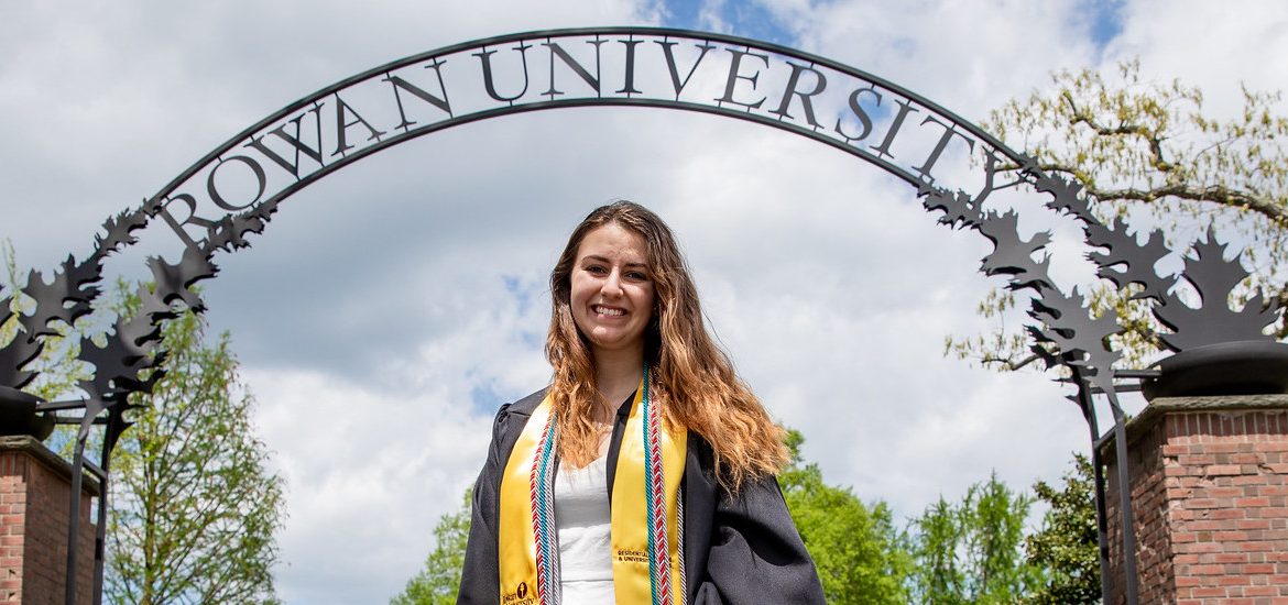 Alyssa smiles and stands in front of the Rowan arch.