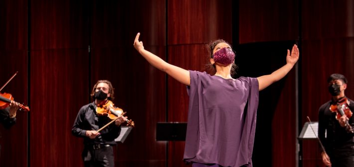 Amanda dancing on stage in a purple outfit and mask with the ensemble around her.