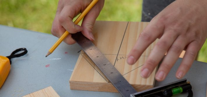 Someone measures a line on a piece of wood.