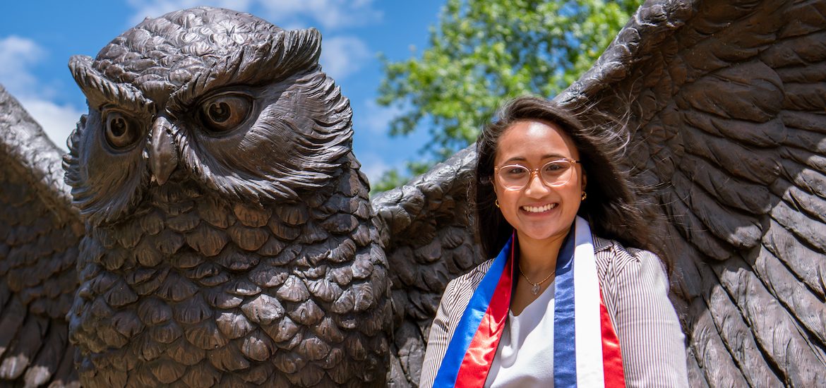 Stephanie sits at the Giant Prof statue on campus while wearing a custom stole showing the Filipino and French flags.