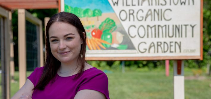 Jenna stands by the entrance sign for the Williamstown Organic Community Garden.