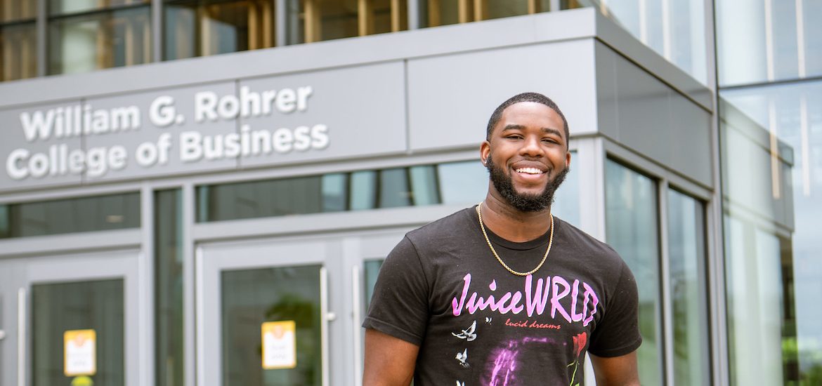 Reshaun smiles and stands in front of the entrance to Business Hall.