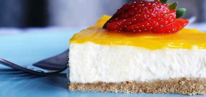 Close up of a slice of white cheesecake with lemon yellow glaze and a strawberry.