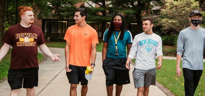 Five students walk and talk on campus.