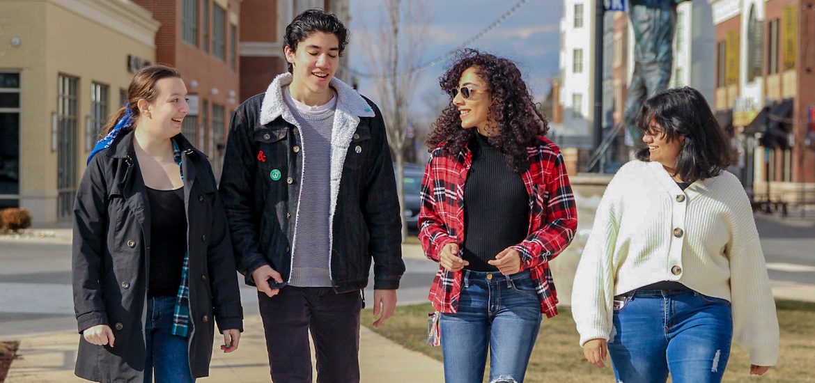 Four students wearing warm autumn clothing walking down a sidewalk on Rowan Boulevard.