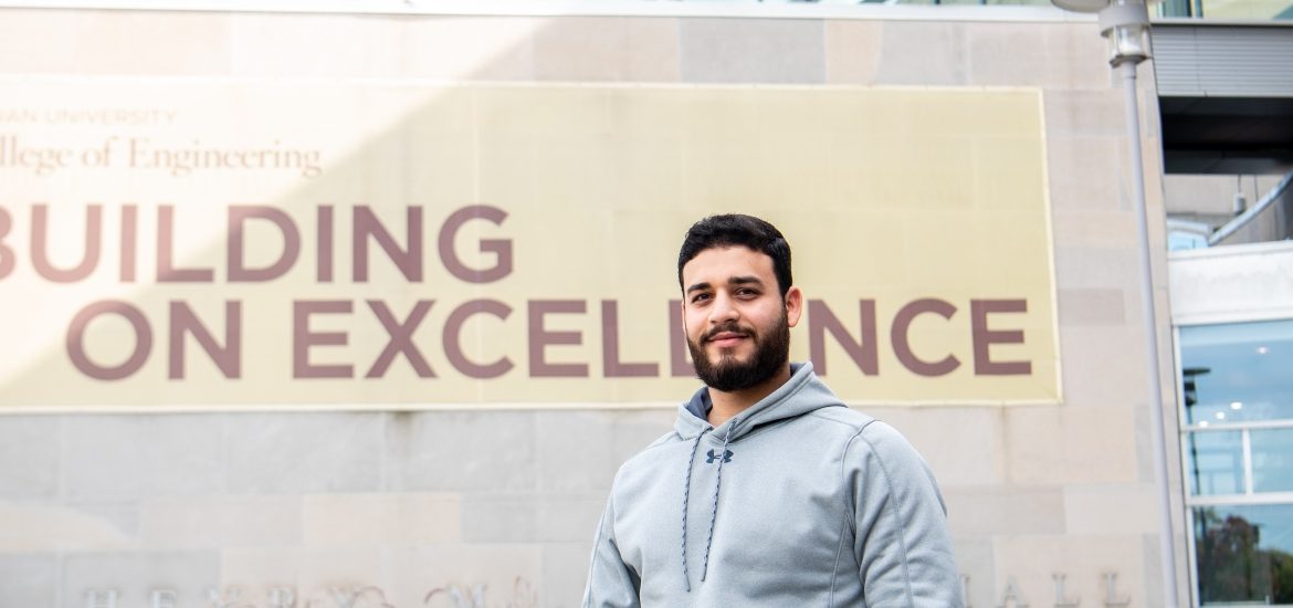 Omar stands in front of the banner at Rowan Hall.