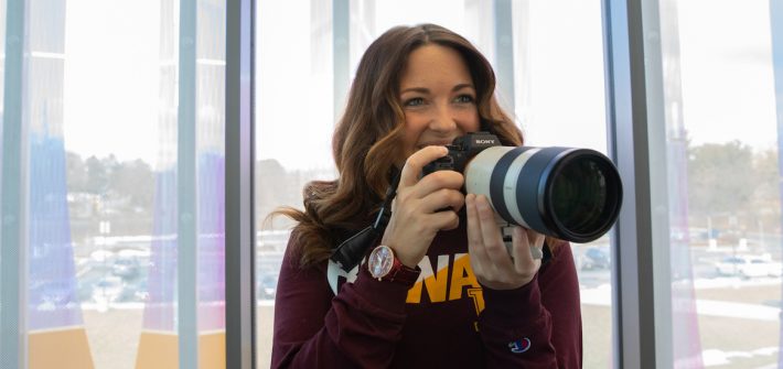 Ashley holds a DSLR camera with a long lens inside Business Hall.