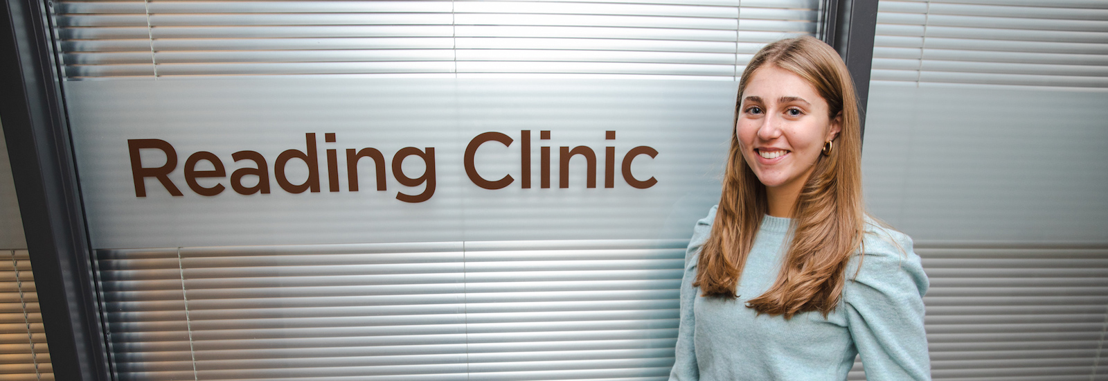 Rowan College of Education student Isabella stands next to the Reading Clinic room inside James Hall.