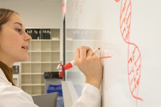 Rowan University Biological Sciences major Mia Shute writes on a whiteboard in the lab.