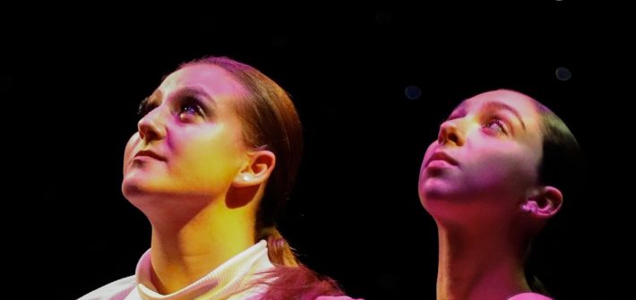 A close up of two dancers faces as they look serious, faces upturned.