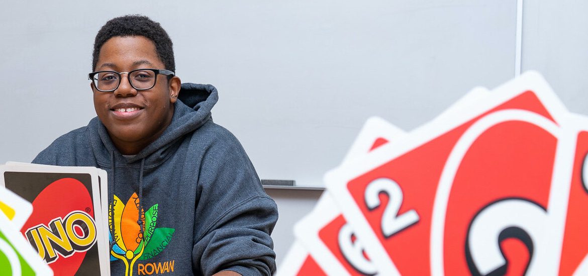 Sedrick is playing Uno with friends and is smiling at the camera.