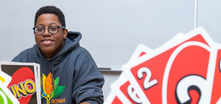 Sedrick is playing Uno with friends and is smiling at the camera.