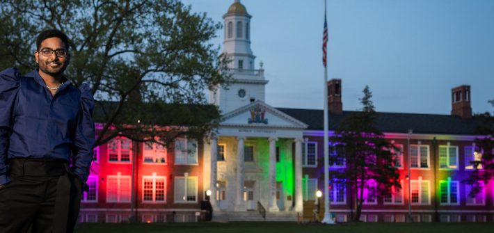 Yash stands in front of the rainbow lights shining on iconic Bunce Hall at night.