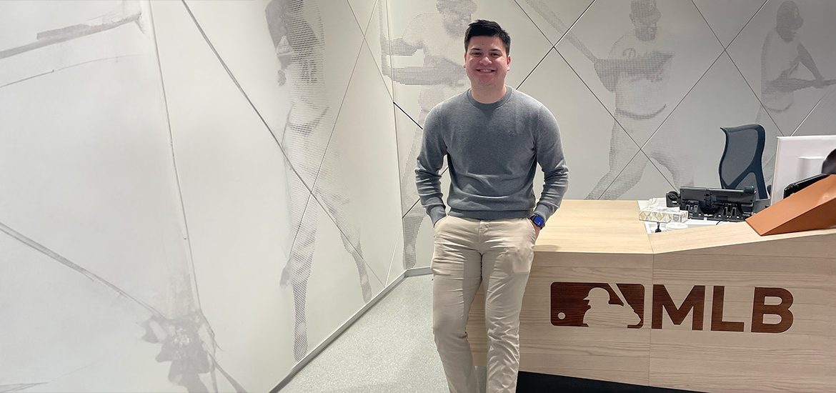 A student standing in front of a Major League Baseball work desk.
