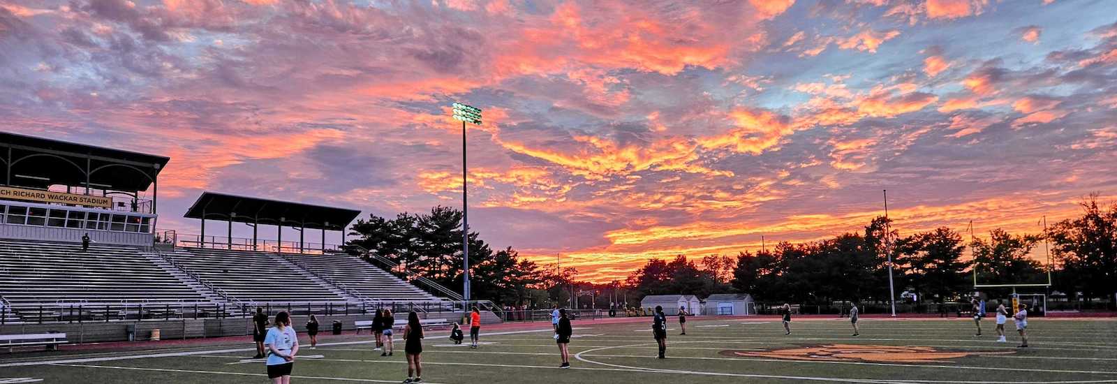 Dramatic sunset photo over the athletic field with the marching band on the field at Rowan University.