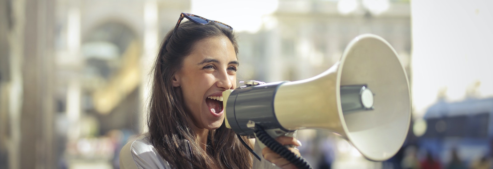 Stock image of a woman happily holding a megaphone to share a message.