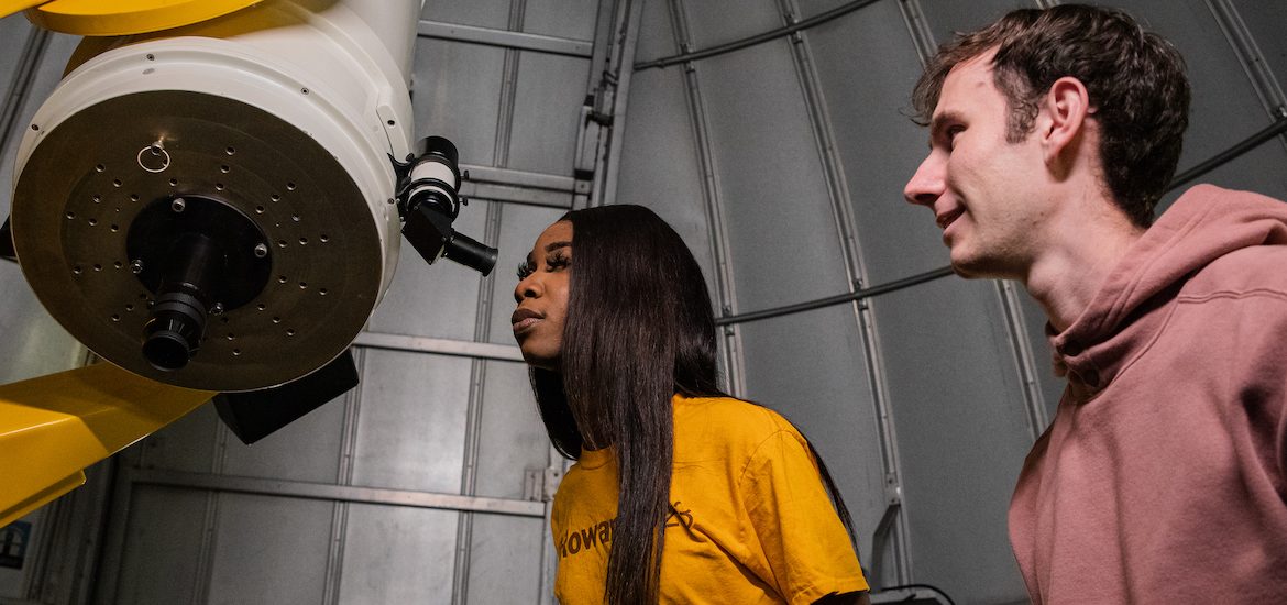 Two students peer into a giant telescope in the planetarium.